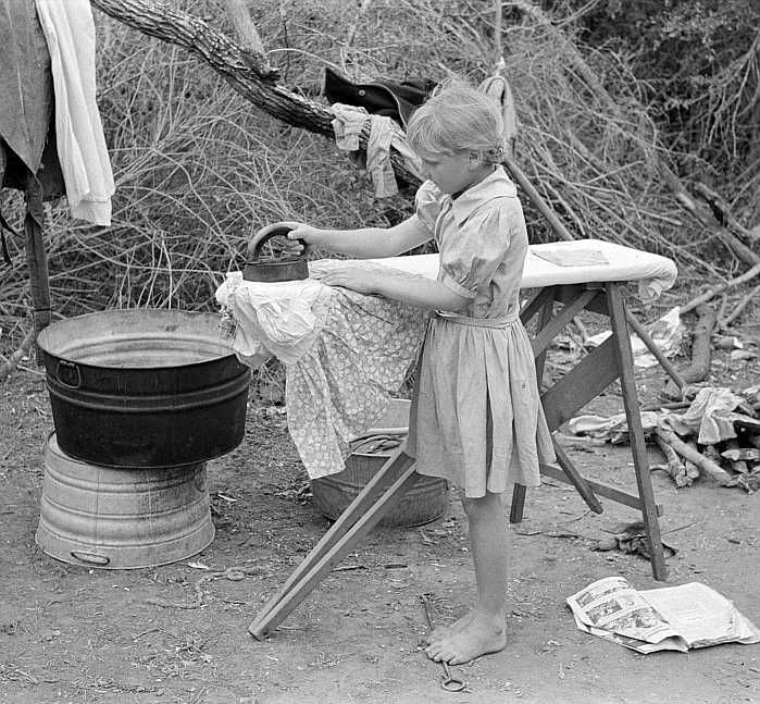 Child of migrant worker ironing in camp near Harlingen, Texas Photo: Russell Lee
